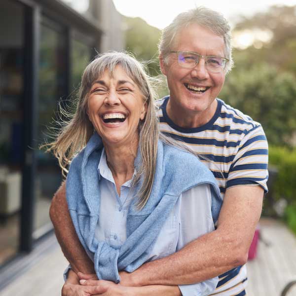 Mature couple standing arm in arm and laughing outside in summer
