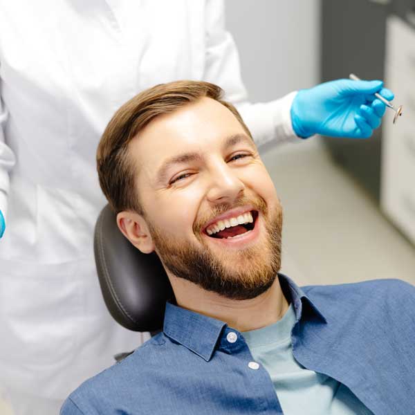 Portrait of happy man sitting at dentist chair in modern clinic and smiling